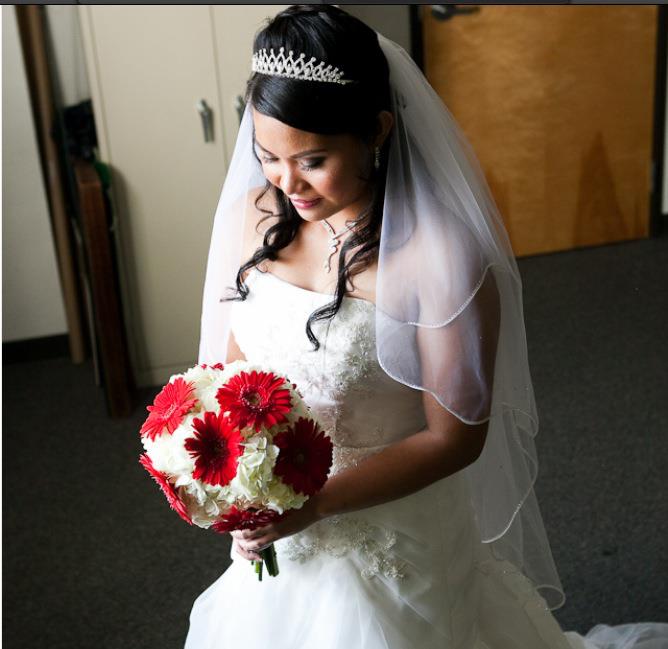 Bride in white dress holding red and white flowers, wearing tiara and veil.