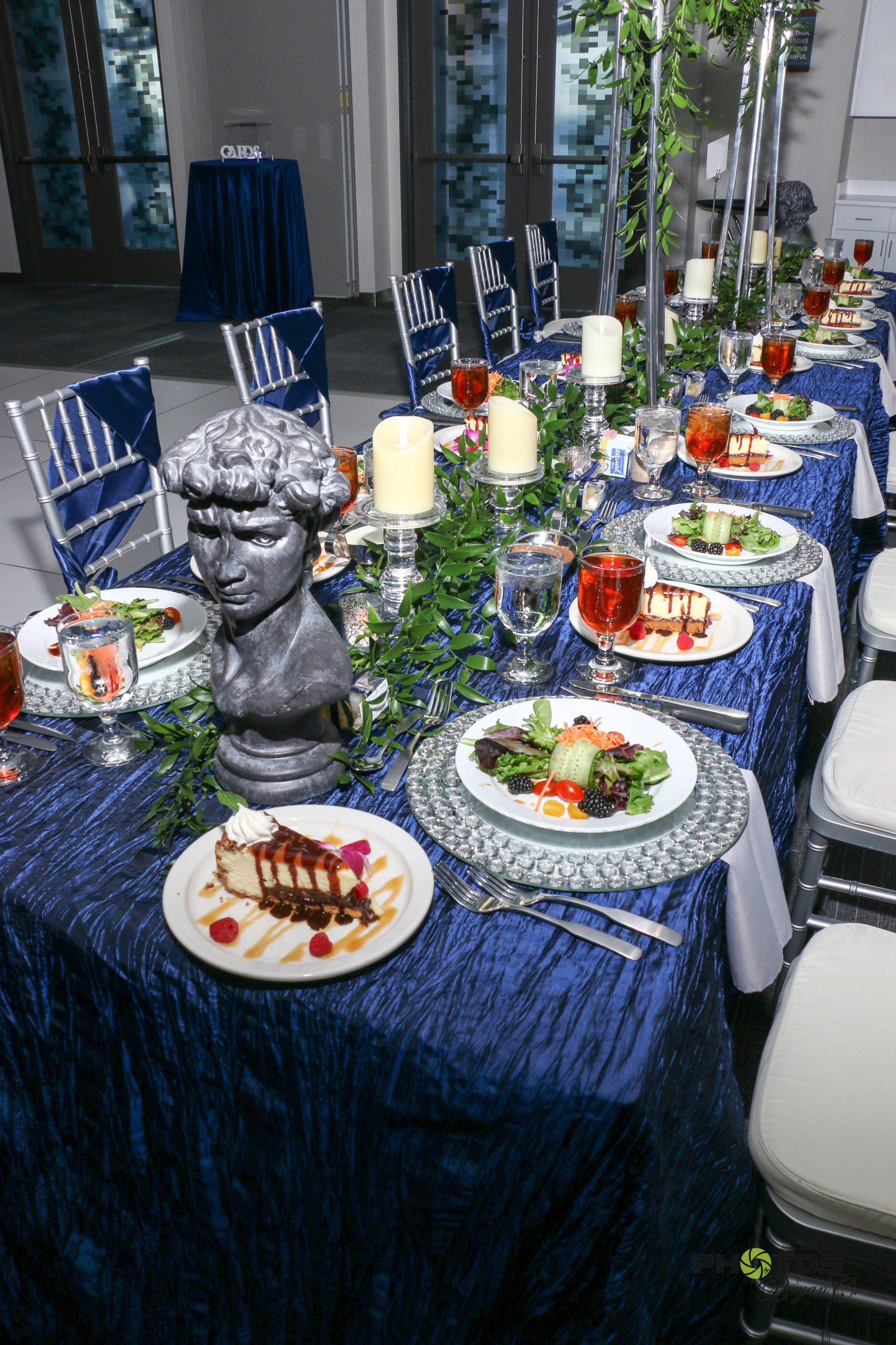 Formal dining table set for event with dark blue tablecloth and decorative centerpieces.