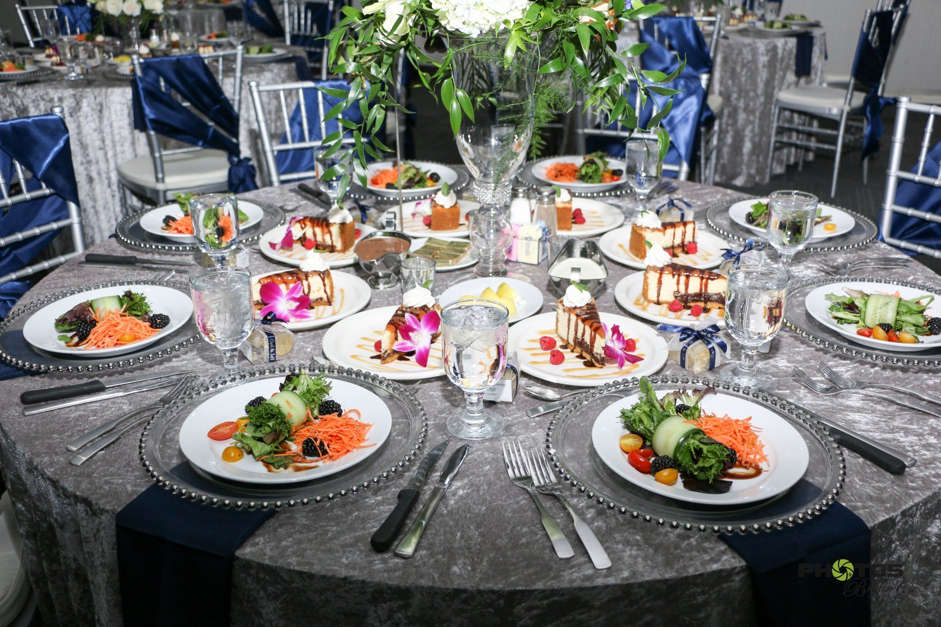 Elegant dining table set for a formal event with plates of food and drinks. Silver tablecloth with blue accents.