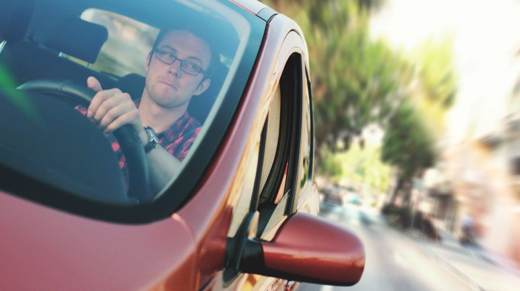 A man is driving a red car down a city street.