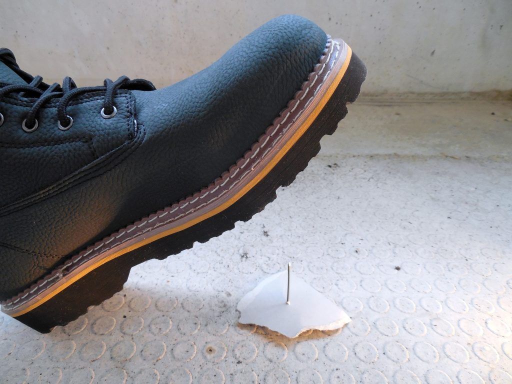 A person 's foot is stepping on a piece of paper with a nail sticking out of it