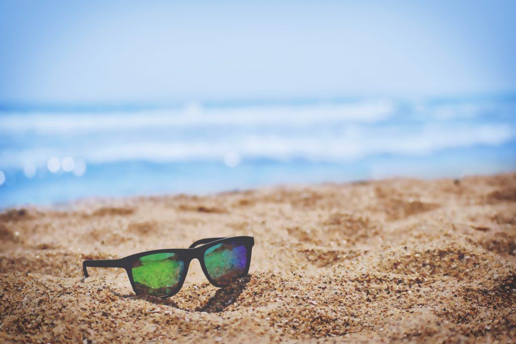 A pair of sunglasses is sitting in the sand on a beach.