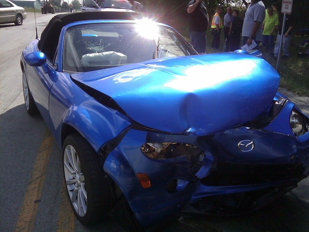 A blue car with a damaged front end is parked on the side of the road