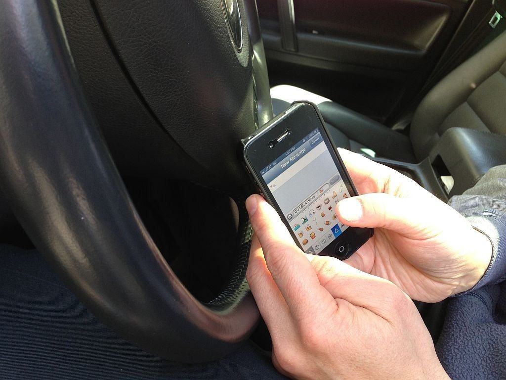 A person is typing on a cell phone in a car