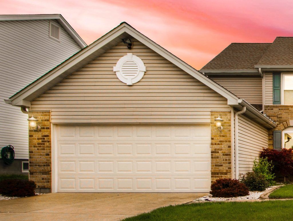 A house with a white garage door and a pink sky in the background.