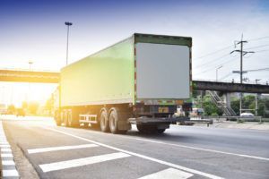 A green semi truck is driving down a highway.