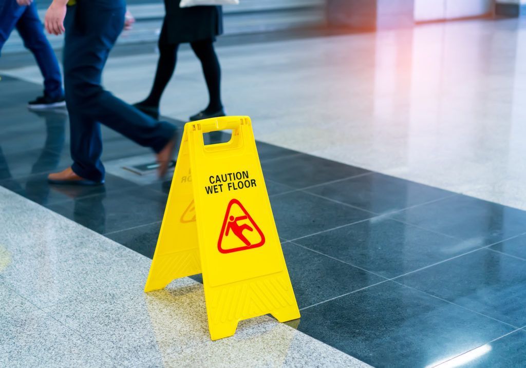 A yellow caution sign on a tiled floor with people walking in the background.