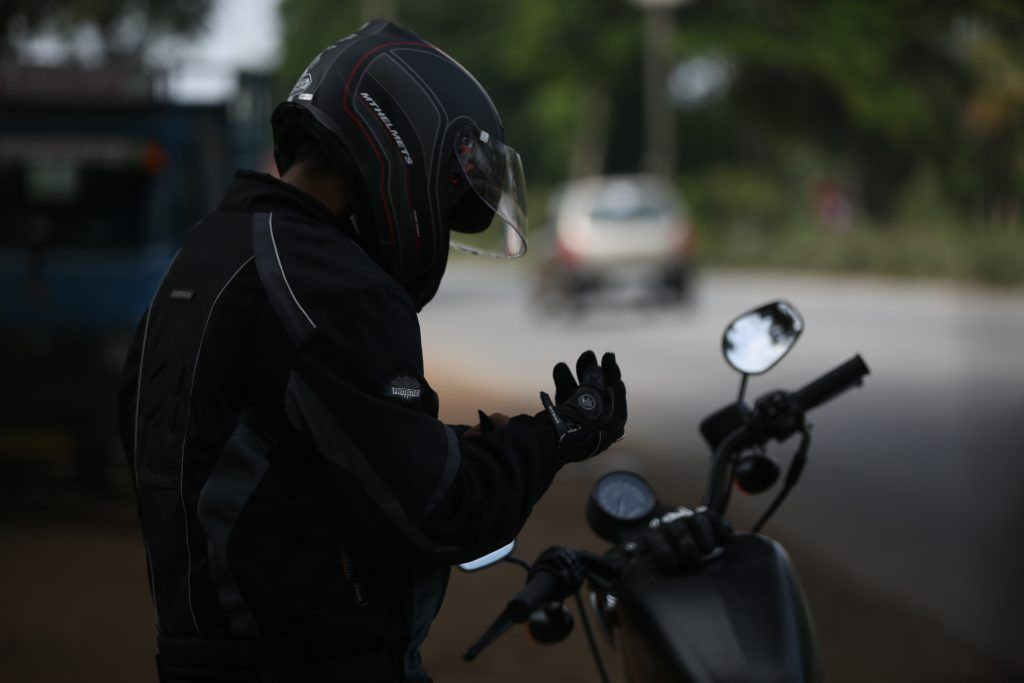 A man wearing a helmet and gloves is standing next to a motorcycle.