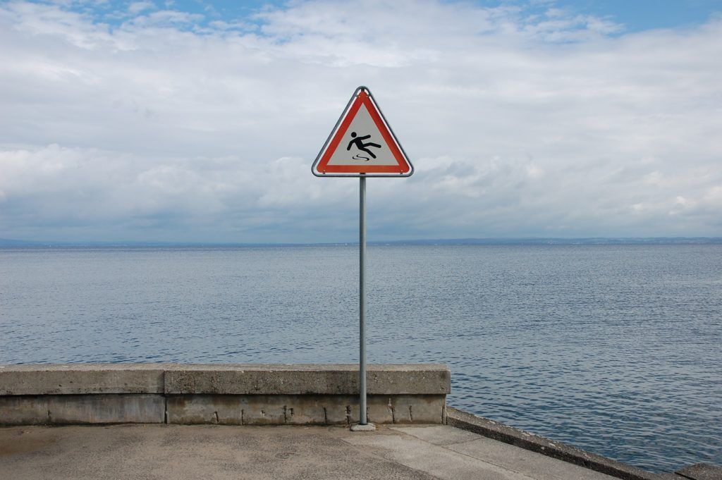 A caution sign on a pole in front of a body of water.