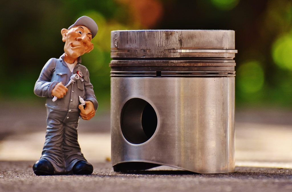 A figurine of a mechanic is standing next to a piston.
