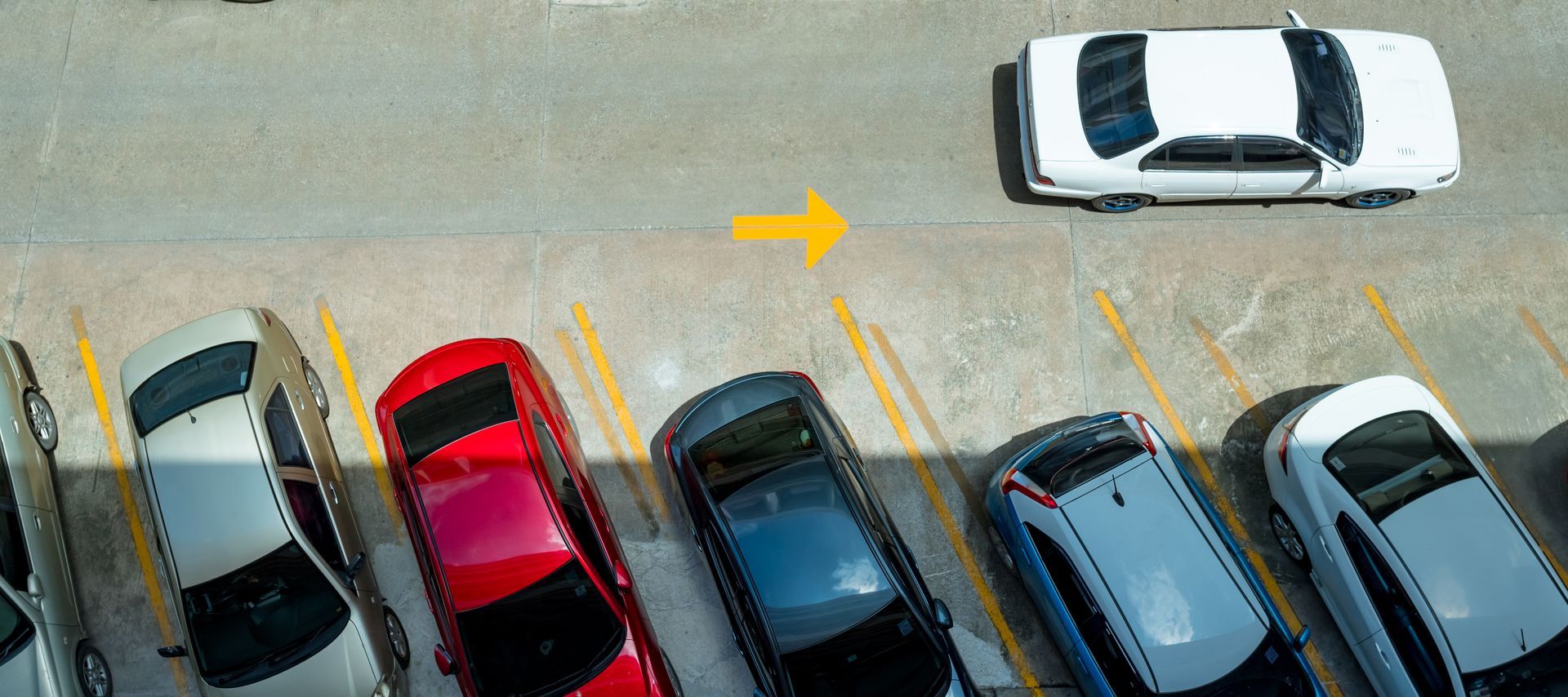 A row of parked car by a white car driving in a parking lot