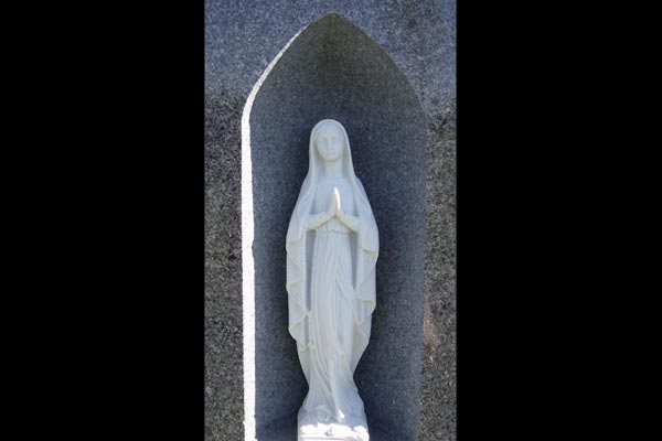 A statue of the virgin mary is carved into a stone wall.