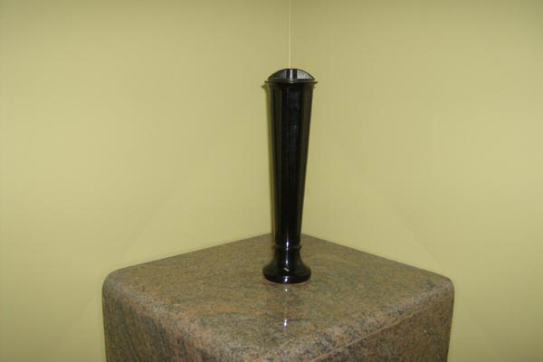 A black vase is sitting on top of a granite pedestal.