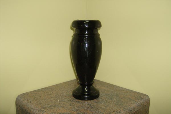 A black vase is sitting on a table in a corner.