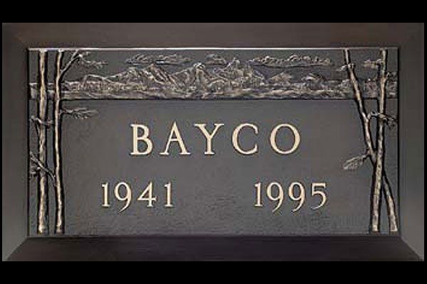 A gravestone for bayco from 1941 and 1995 with trees in the background.