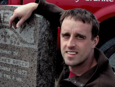 A man leaning against a gravestone that says ' memorial of owen goper ' on it