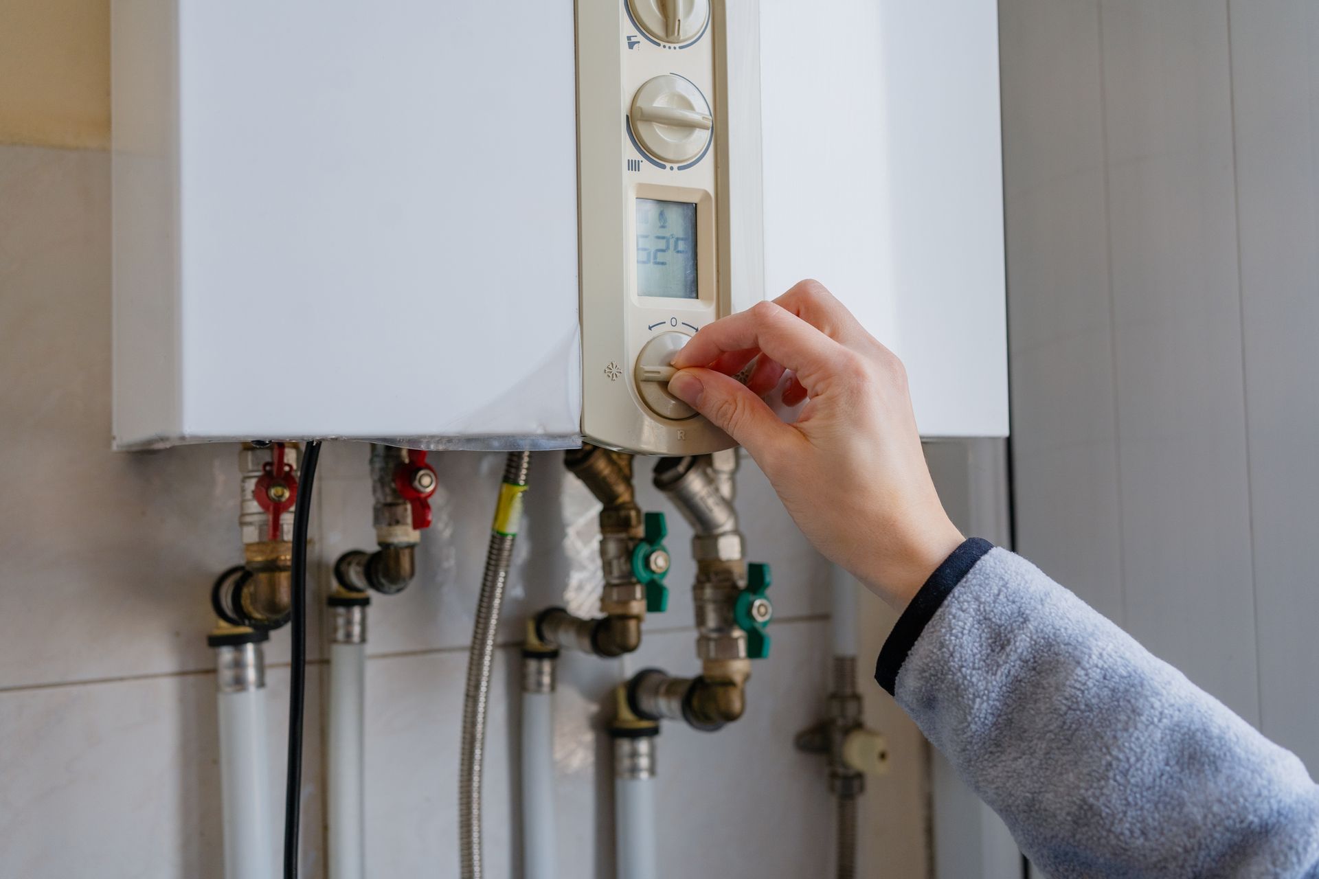 Hand adjusting a wall-mounted boiler control knob among exposed pipes and valves Hand adjusting a wall-mounted boiler control knob among exposed pipes and valves