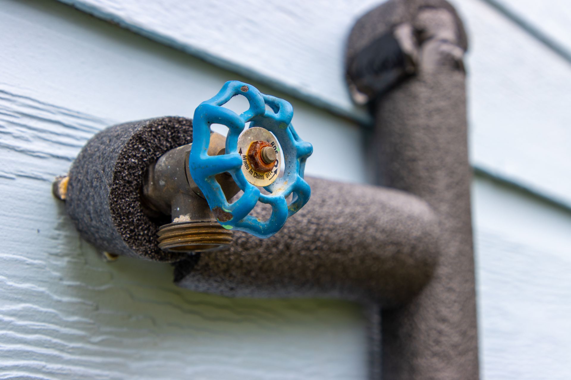 Blue outdoor faucet handle on an exterior wall, with a black insulated pipe and hose attached. Blue outdoor faucet handle on an exterior wall, with a black insulated pipe and hose attached.