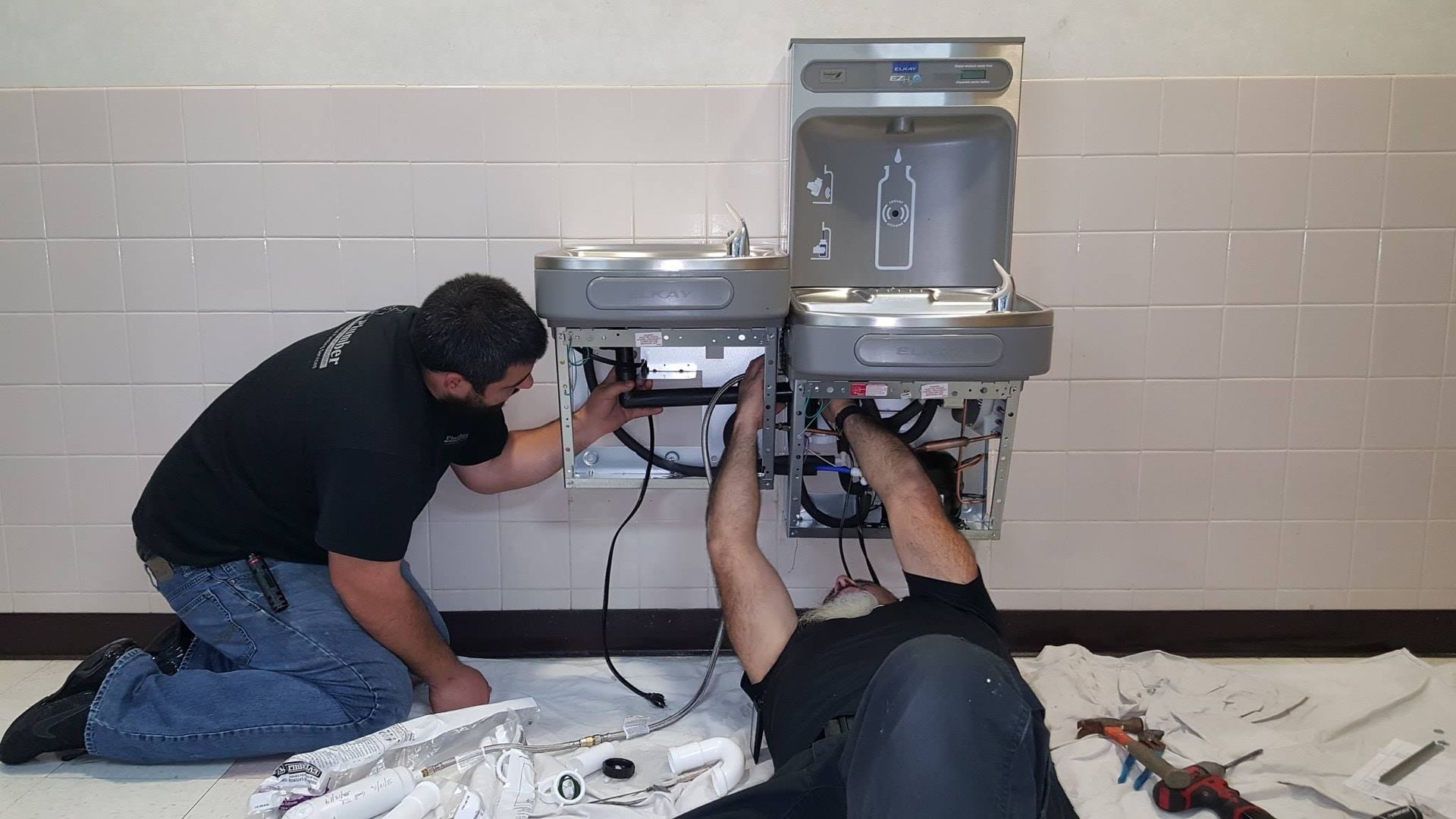 Plumber tightening a pipe connection under a sink with exposed plumbing and tools nearby