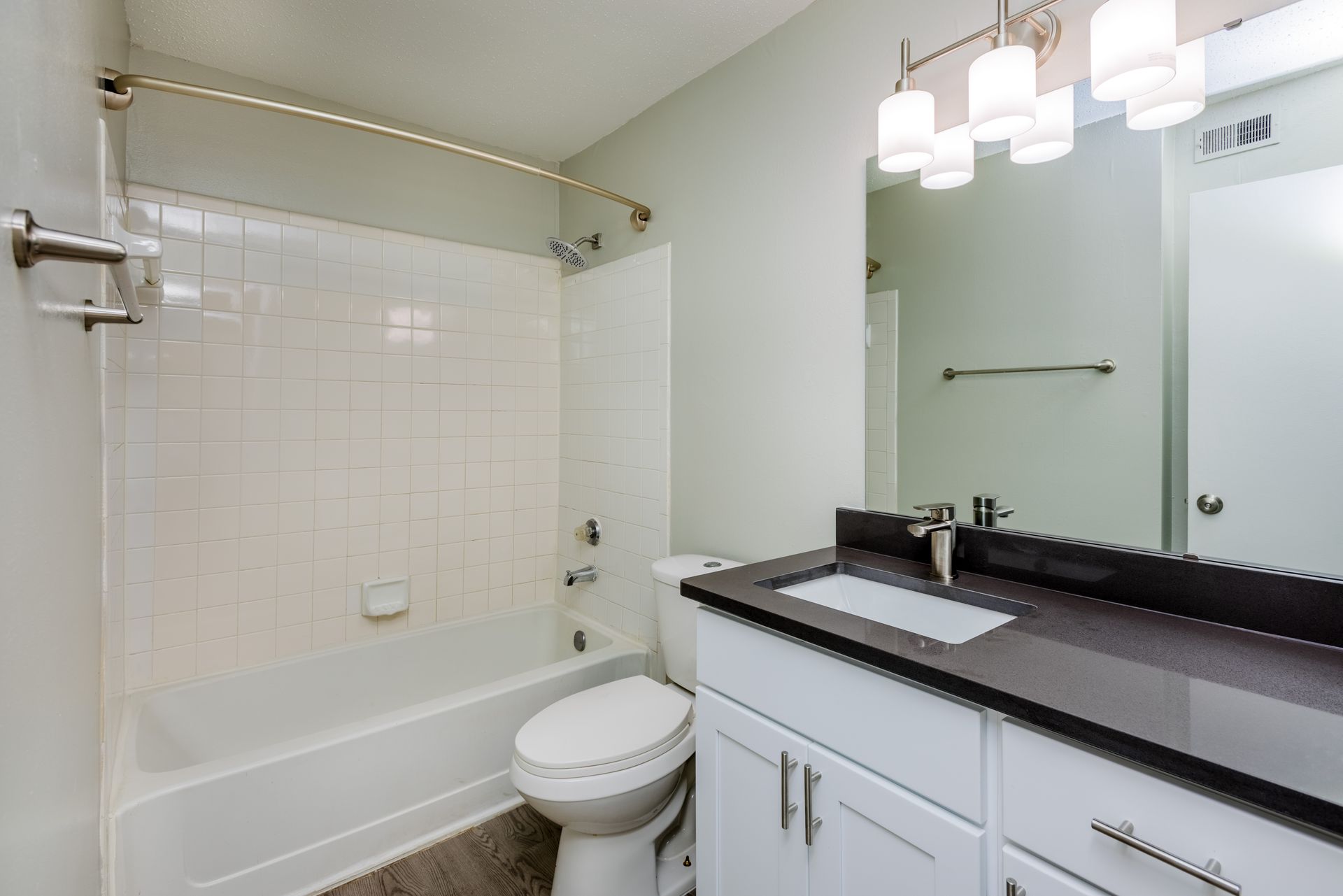 Bathroom with white tile shower/tub, toilet, white vanity, dark countertop, and large mirror. Contact us today to take a tour of our 1, 2, and 3-bedroom apartments for rent in Charlotte, NC.