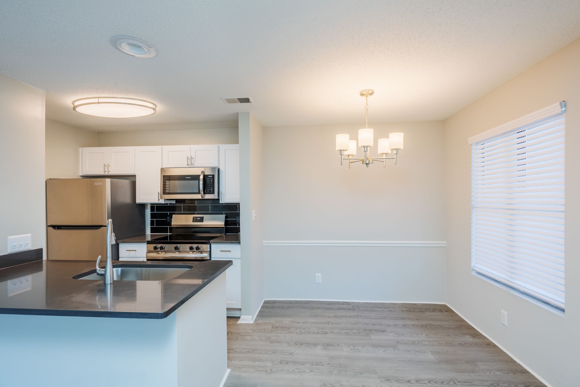 Open-plan kitchen and dining area with stainless steel appliances, dark countertop, white cabinets, and a chandelier. Contact us today to take a tour of our 1, 2, and 3-bedroom apartments for rent in Charlotte, NC.