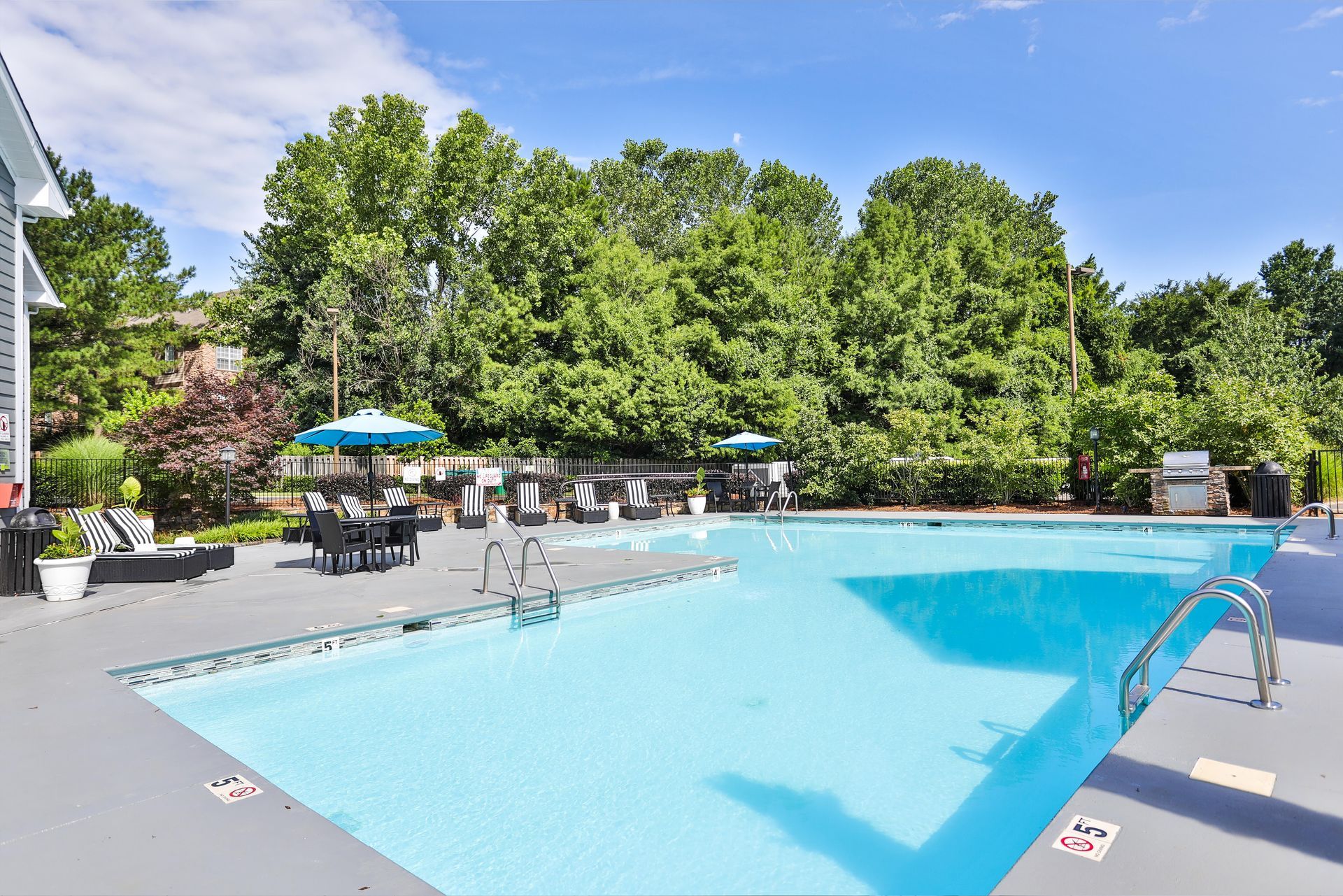Swimming pool with turquoise water, surrounded by a gray deck and trees under a blue sky. Our apartments in Charlotte, NC offer a convenient location and top-notch amenities. Call today to schedule your tour!