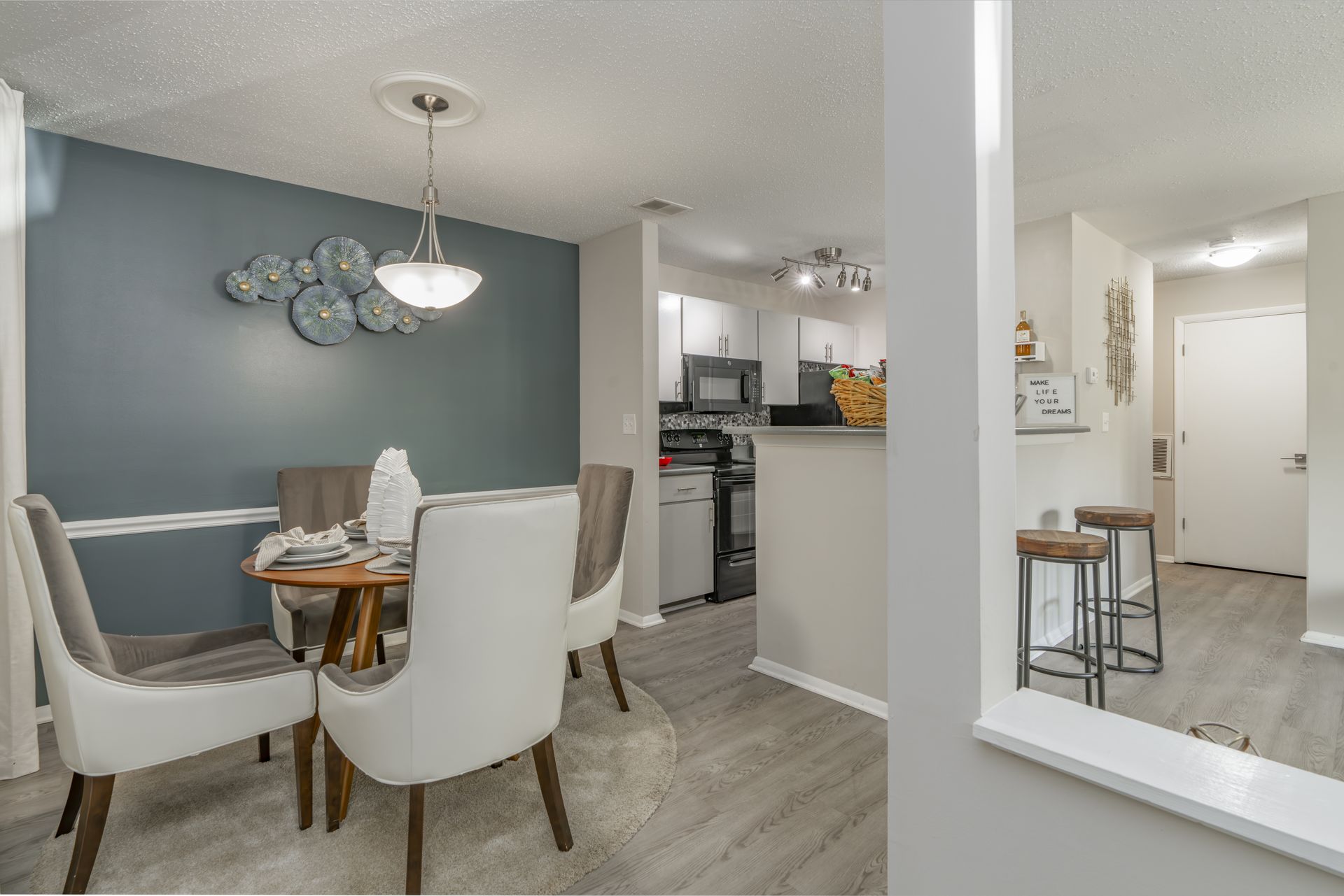 Dining room with gray walls, round table, chairs, and view into kitchen and hallway. Contact us today to take a tour of our 1, 2, and 3-bedroom apartments for rent in Charlotte, NC.