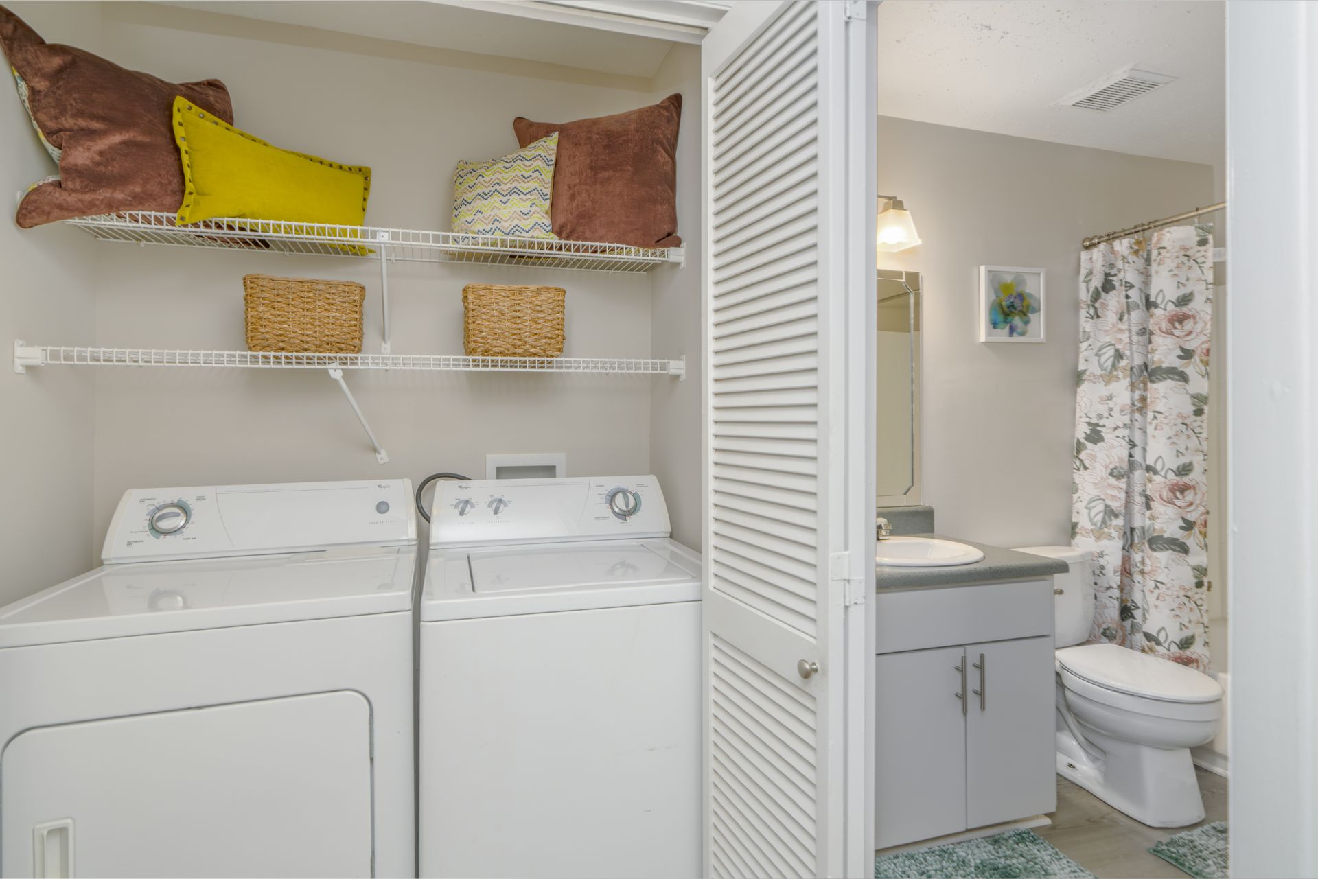 Washer and dryer in a laundry area with shelves. Bathroom visible through the open door. Contact us today to take a tour of our 1, 2, and 3-bedroom apartments for rent in Charlotte, NC.