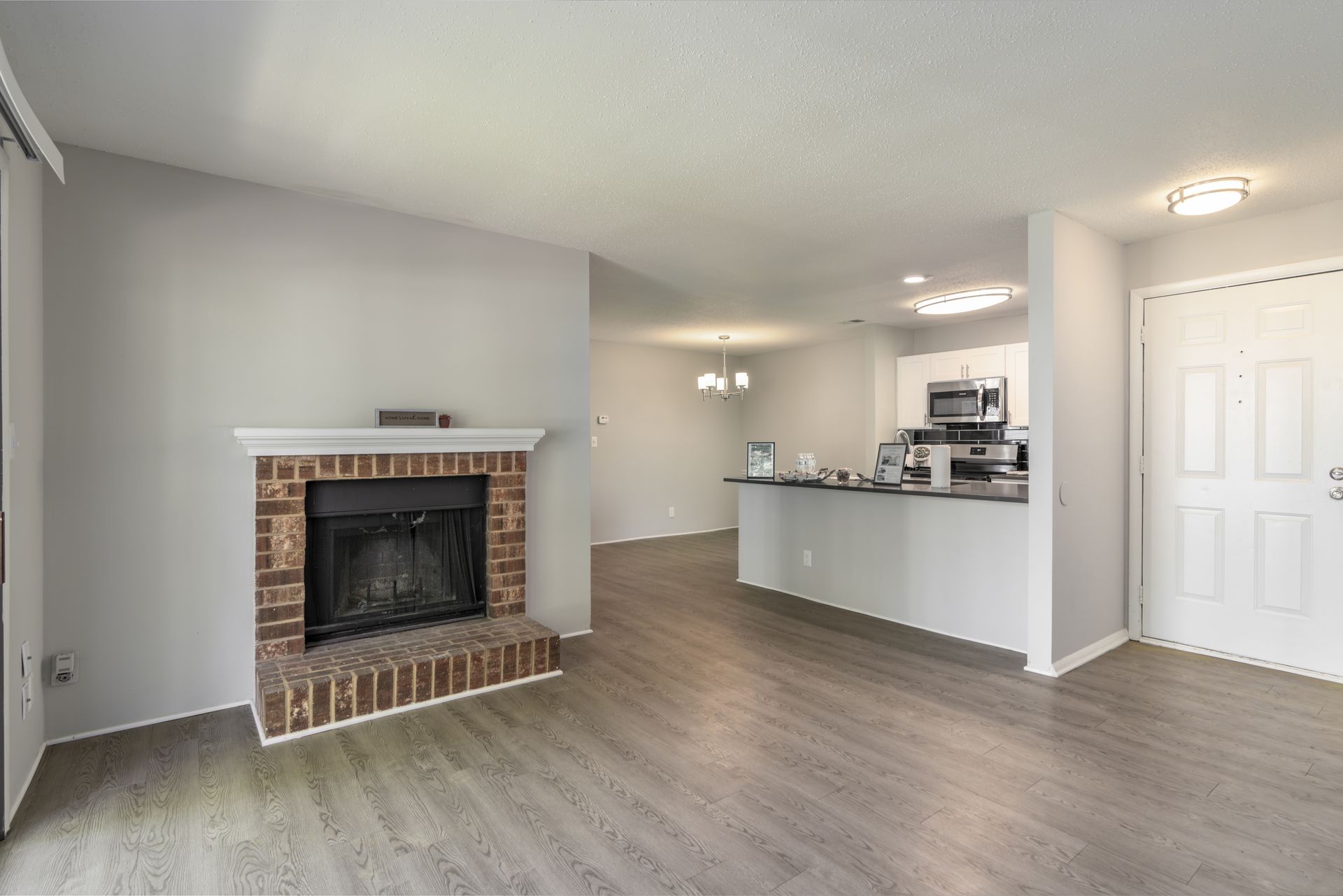 Empty living space with fireplace, kitchen, and doorway. Gray walls, wood-look flooring. Contact us today to take a tour of our 1, 2, and 3-bedroom apartments for rent in Charlotte, NC.