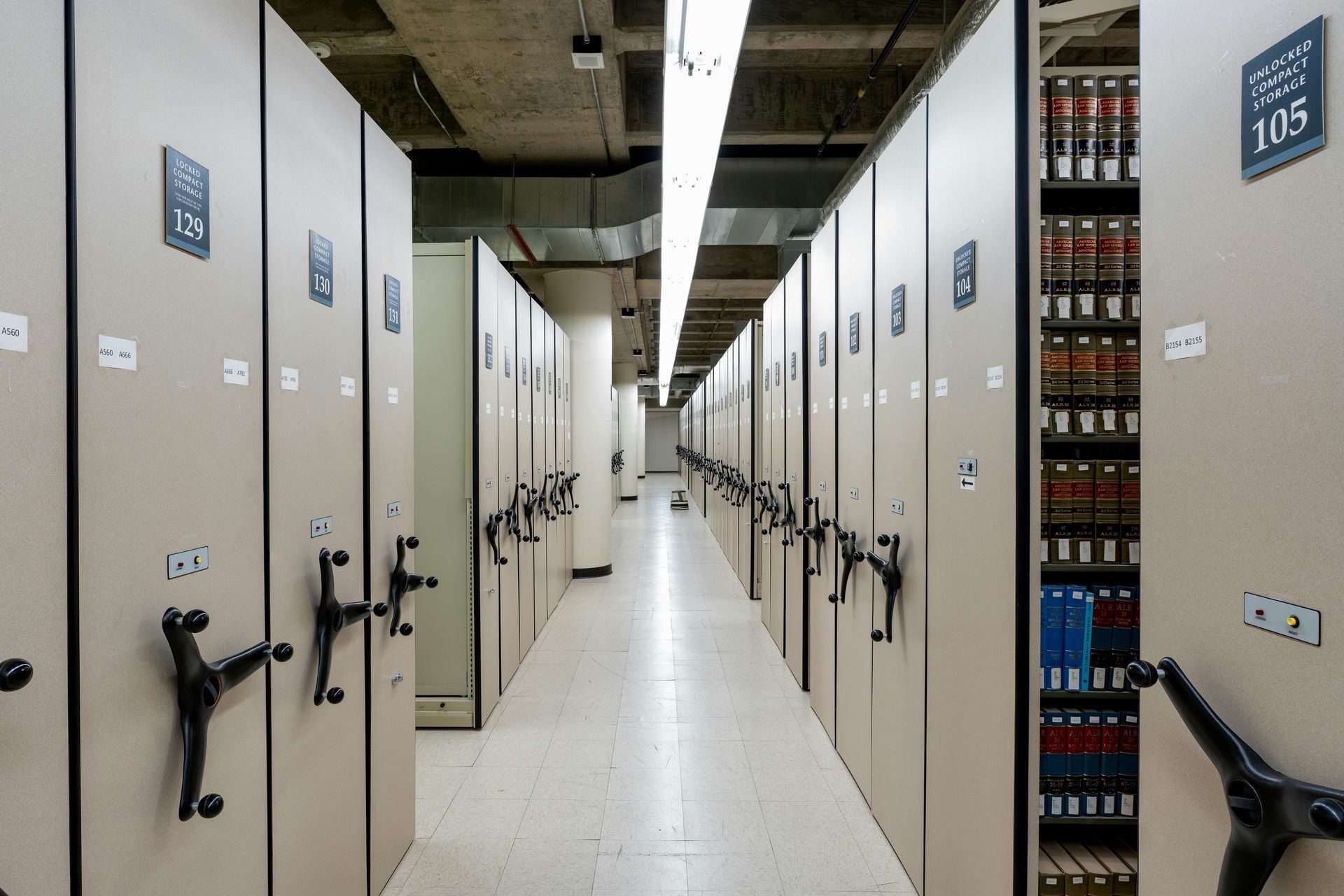 Rows of beige, mobile shelving units in a long, well-lit archive storage area.