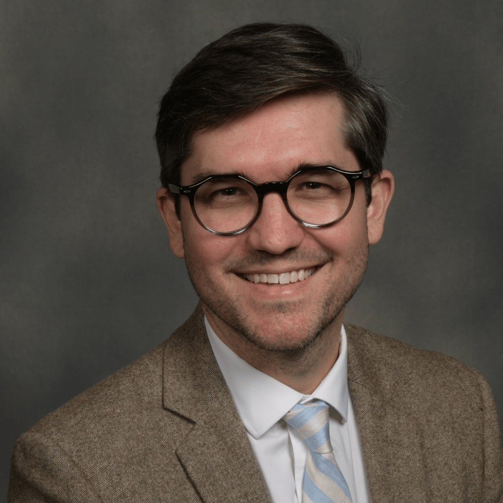 Headshot of Rev. Rex Childs smiling with glasses against a gray background.