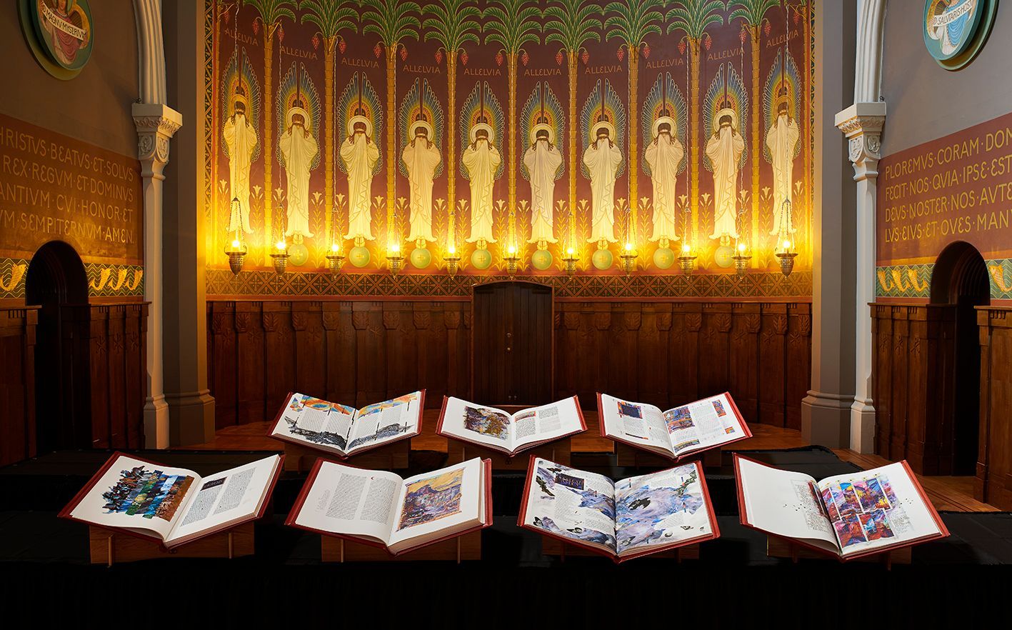 Seven large, open volumes of the Saint John's Bible displayed on a wooden stand in a chapel.