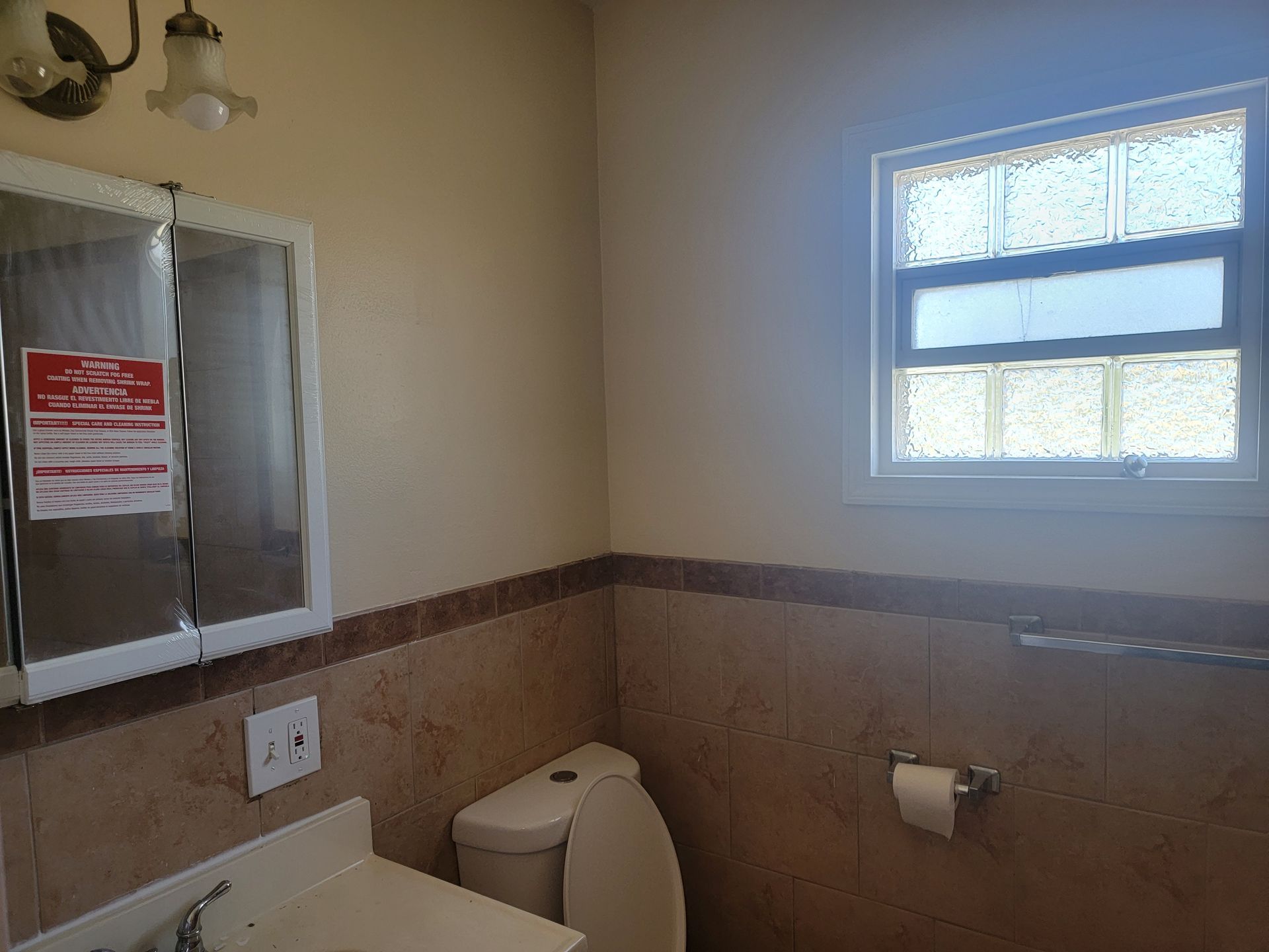 A bathroom with a toilet , sink , mirror and window.