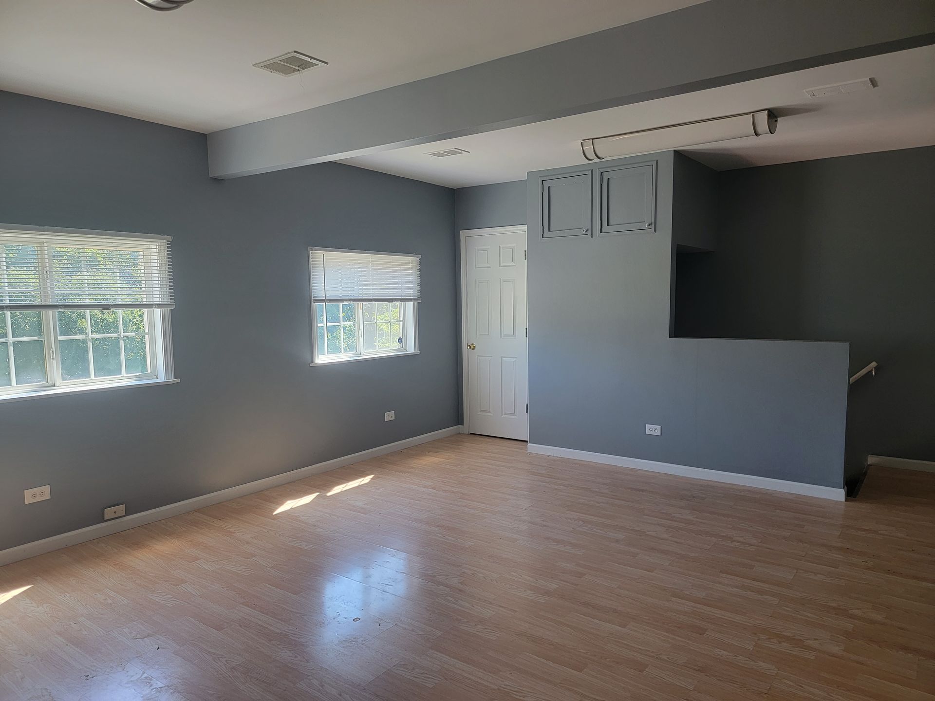 An empty living room with hardwood floors and gray walls.