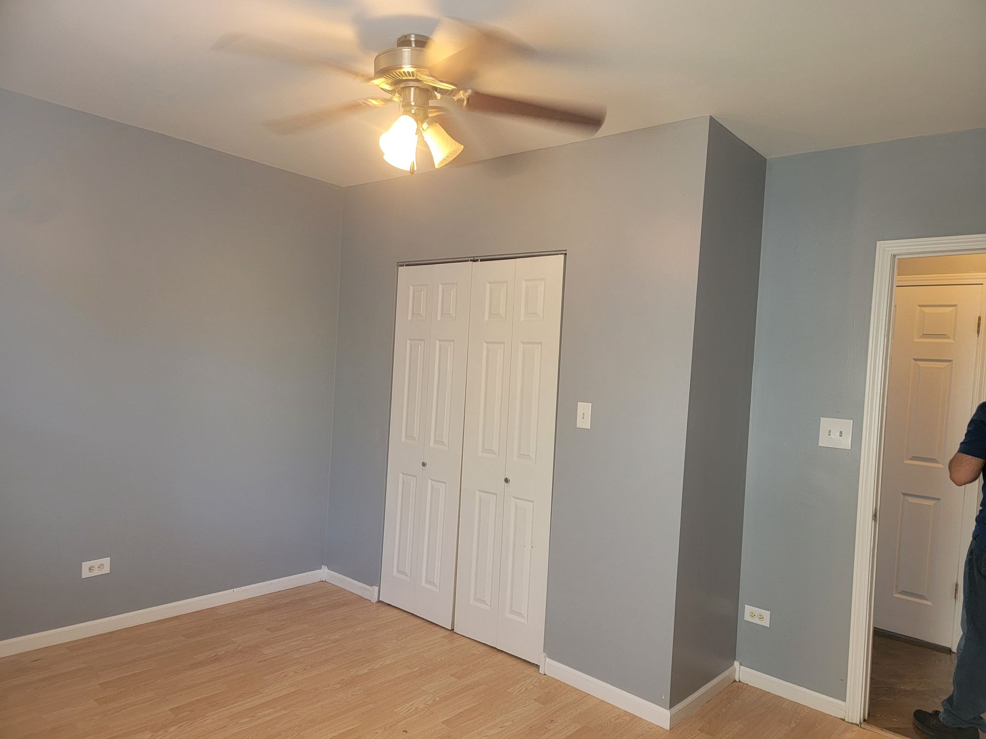 A man is standing in an empty room with a ceiling fan.