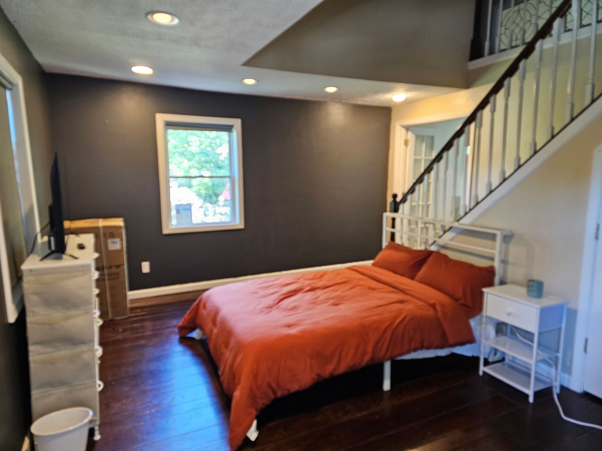 A bedroom with a bed , nightstand , dresser and stairs.