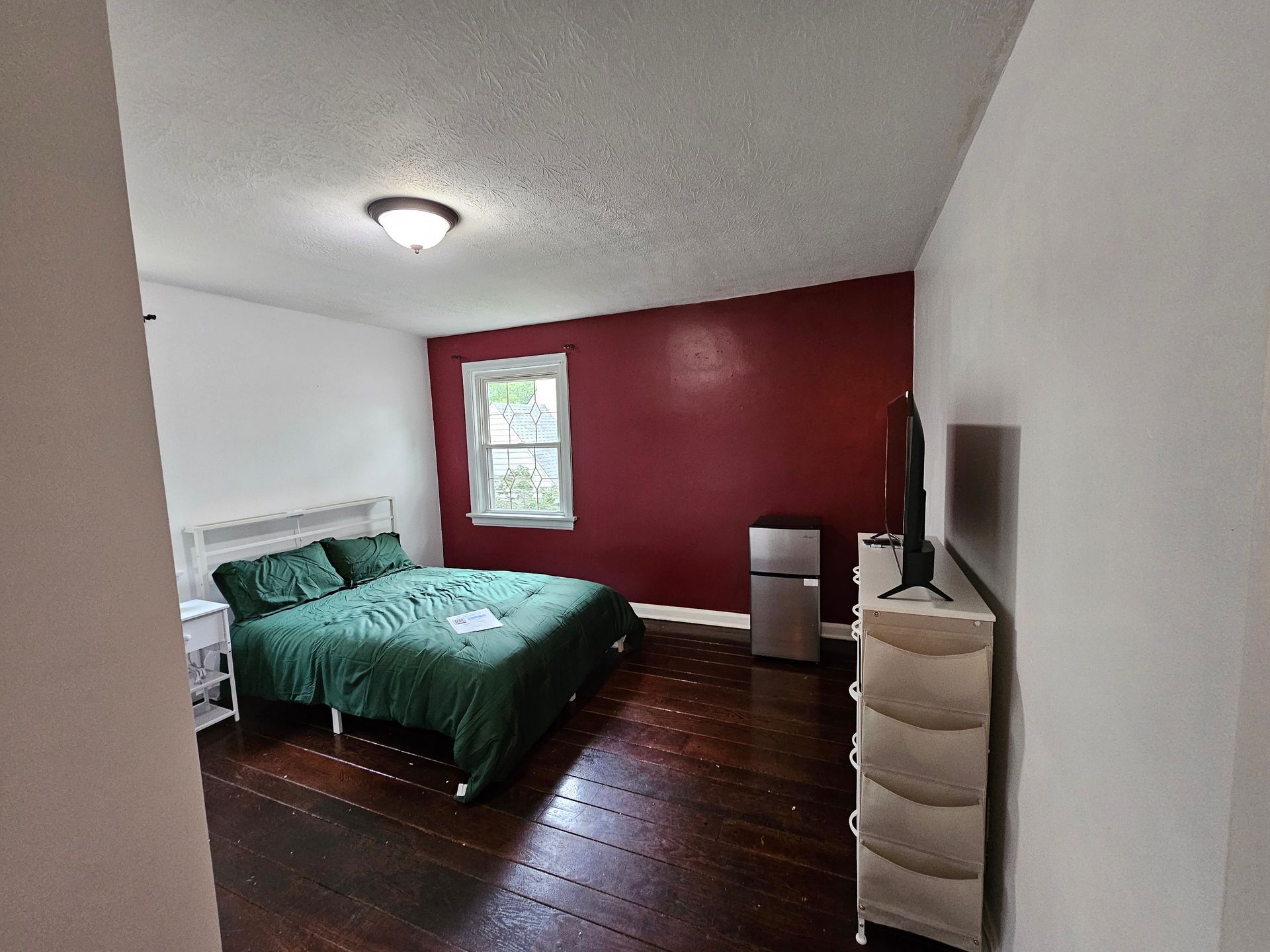 A bedroom with a bed , dresser , refrigerator and television.