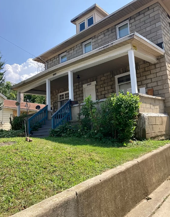 A large brick house with a large porch and stairs leading up to it.