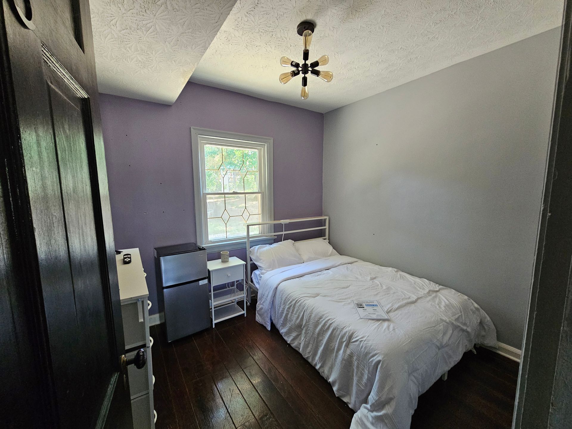 A bedroom with a bed , a refrigerator , and a window.