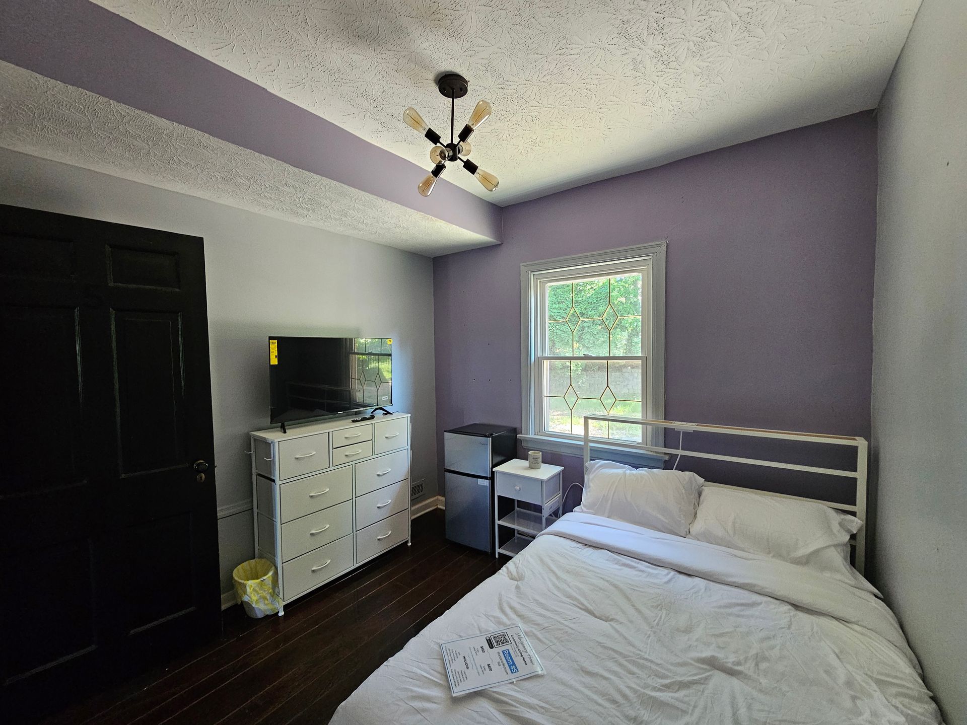 A bedroom with a bed , dresser , refrigerator and television.