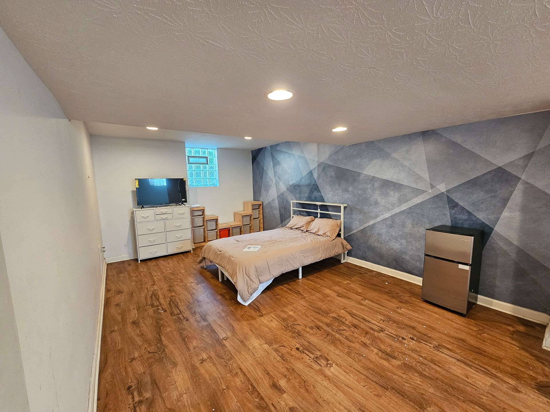 A bedroom with a bed , dresser , television and refrigerator.