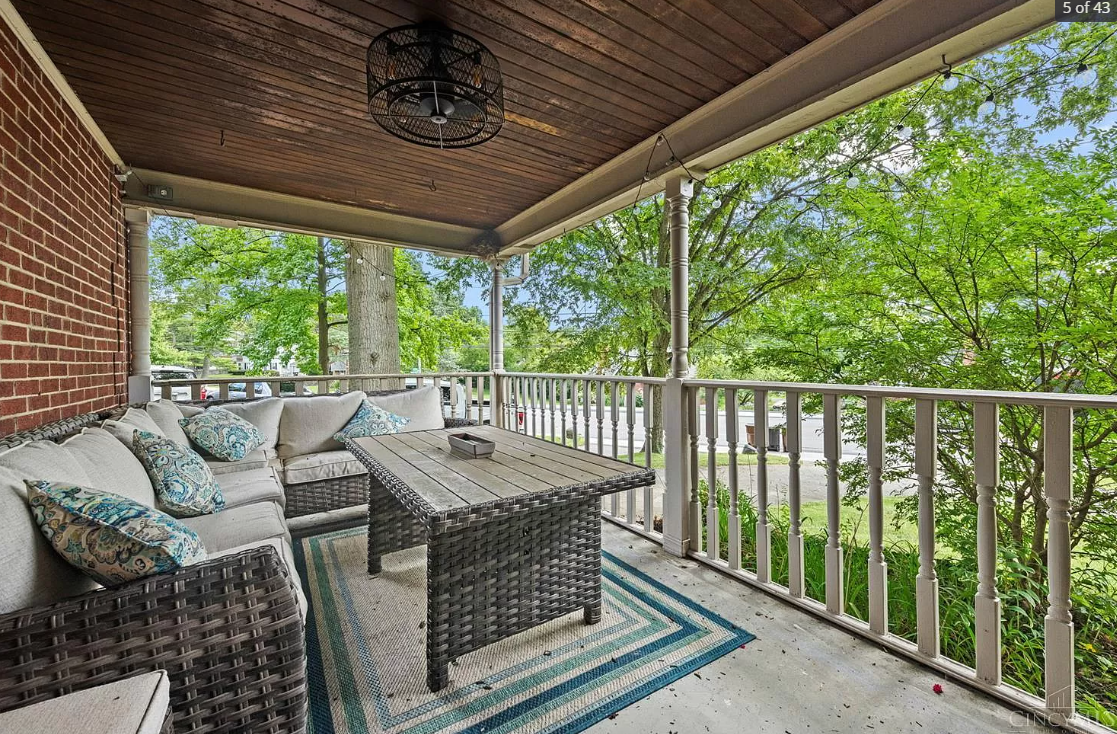 A porch with a couch , table , rug and a ceiling fan.