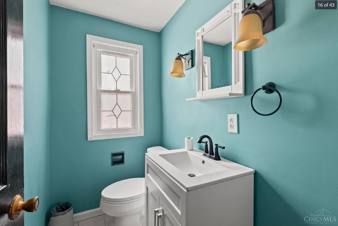 A bathroom with blue walls , a sink , toilet and mirror.