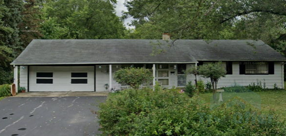 A white house with a black roof is surrounded by trees and bushes.