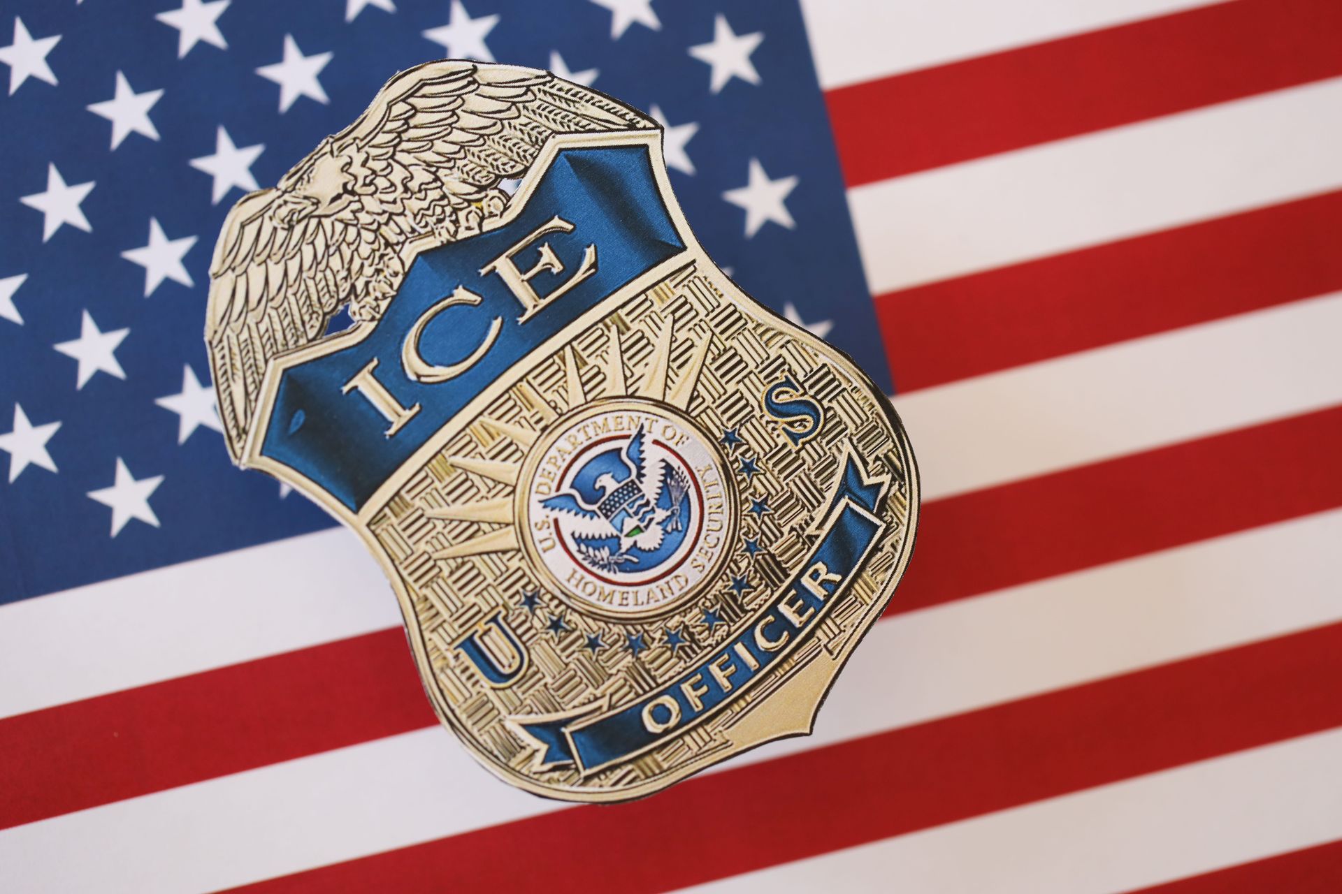 ICE officer badge over a U.S. flag background