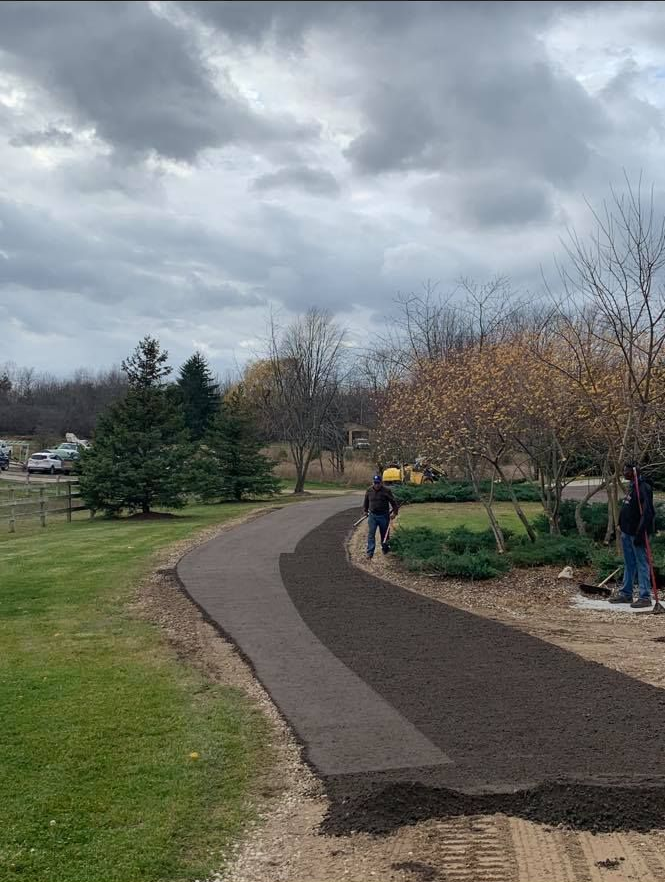 Curving paved path through a park under cloudy skies, with trees and a few people walking.