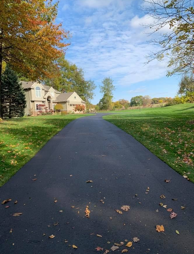 Curved driveway beside a house and autumn trees under a blue sky