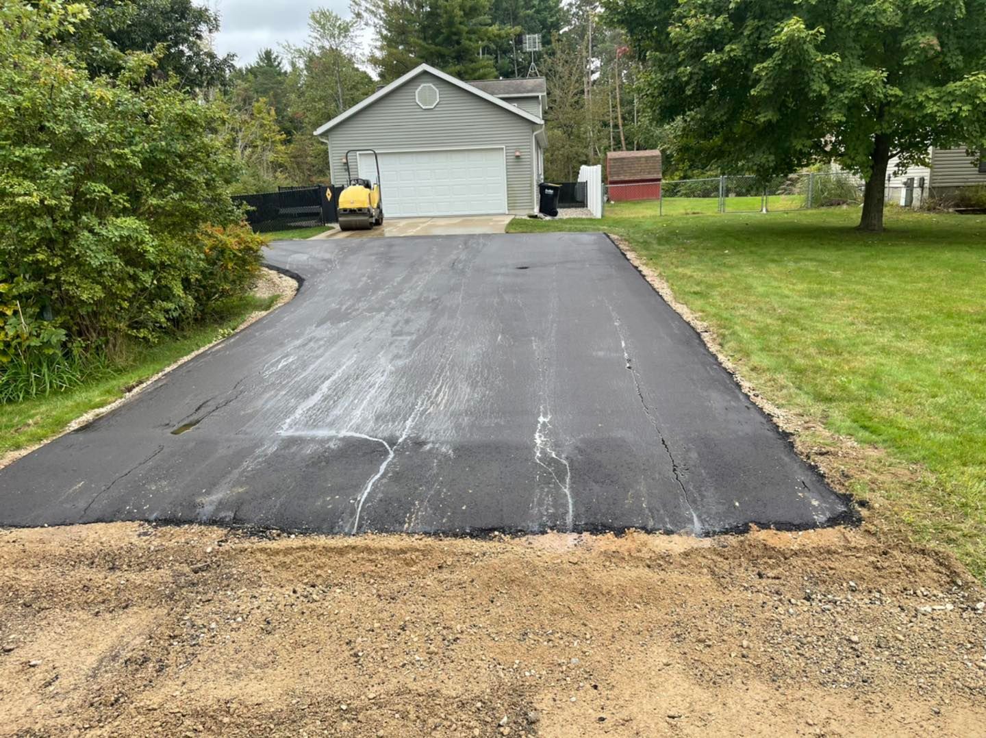 Freshly paved driveway leading to a garage, with a gravel edge in the foreground.