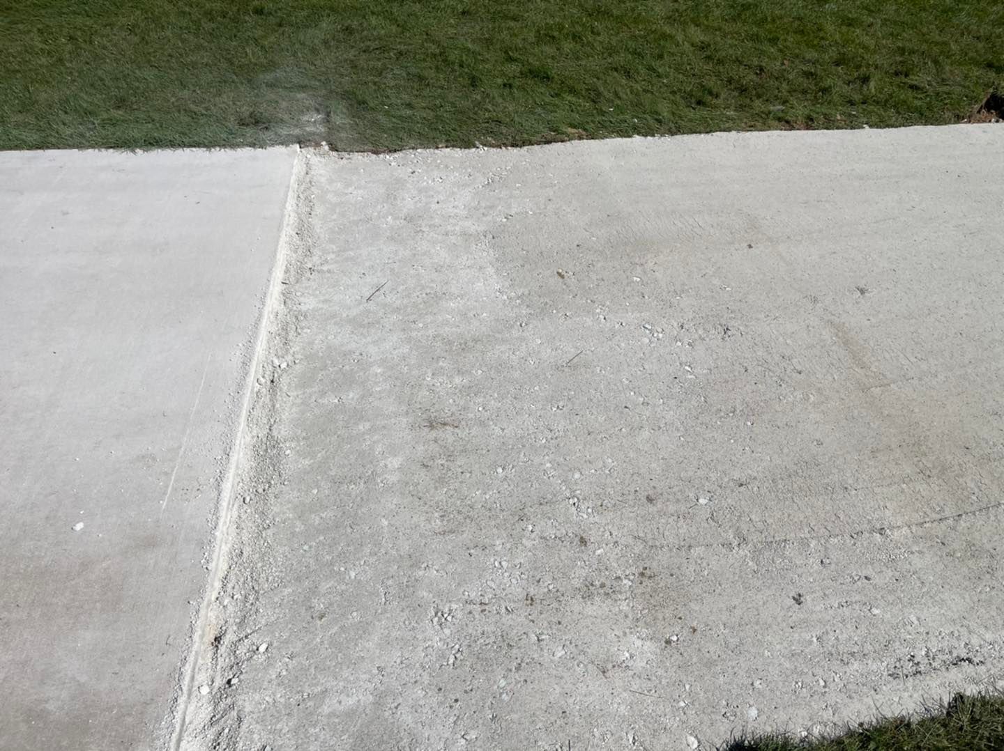 Concrete sidewalk with a seam beside a grassy lawn.