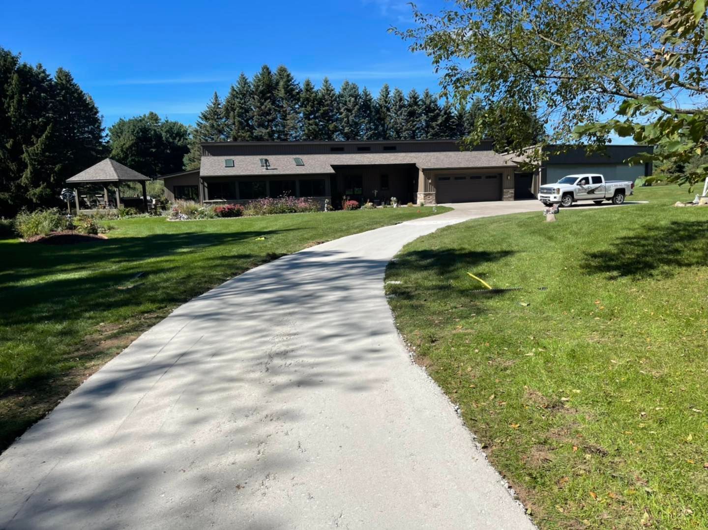 Curved driveway leading to a house with a garage, lawn, trees, and a parked truck on a sunny day